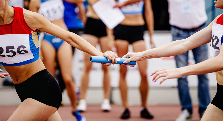 A closeup on the handoff of a blue baton between two runners in a relay race