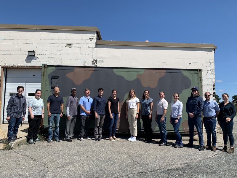 14 researchers pose for a group photo outside. 