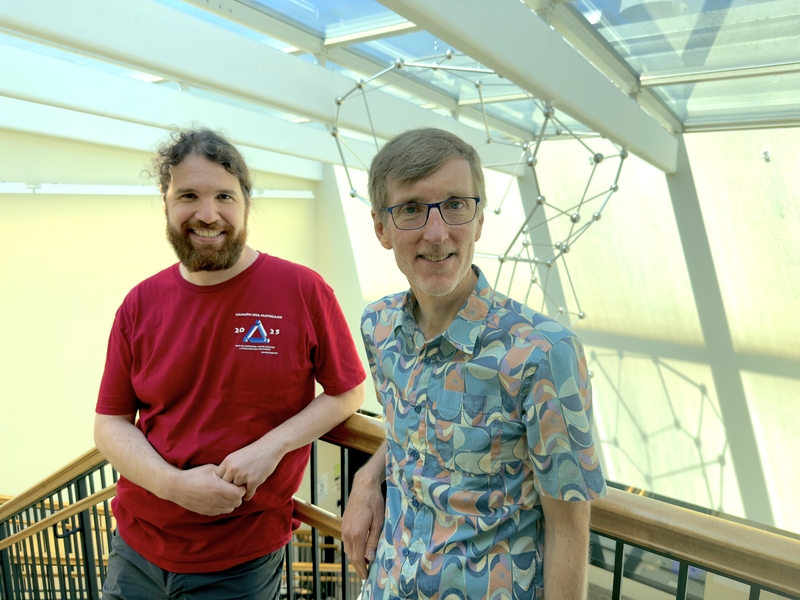 David Roe and Andrew Sutherland leaning against a railing in the Math building