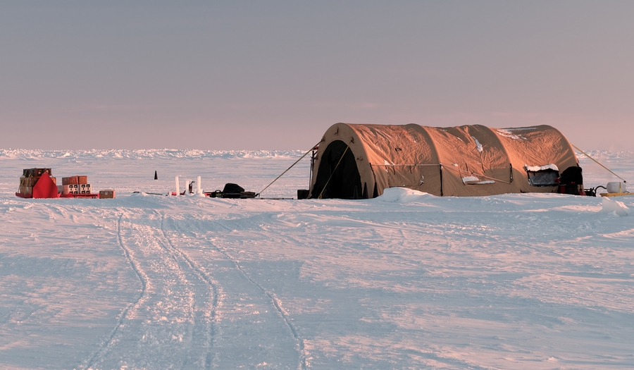 A large tubular tent and supplies sit atop ice in the Arctic. 