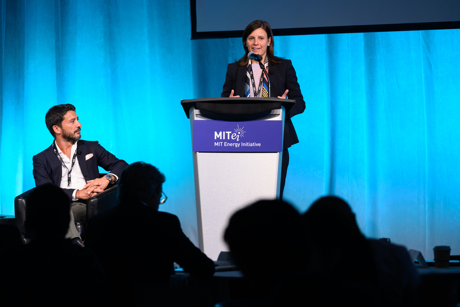 A woman speaks at a lectern while a man seated to her right listens.