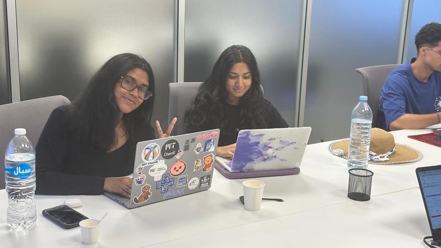 Two women working at their laptops. The one on the left flashes a peace sign at the camera.