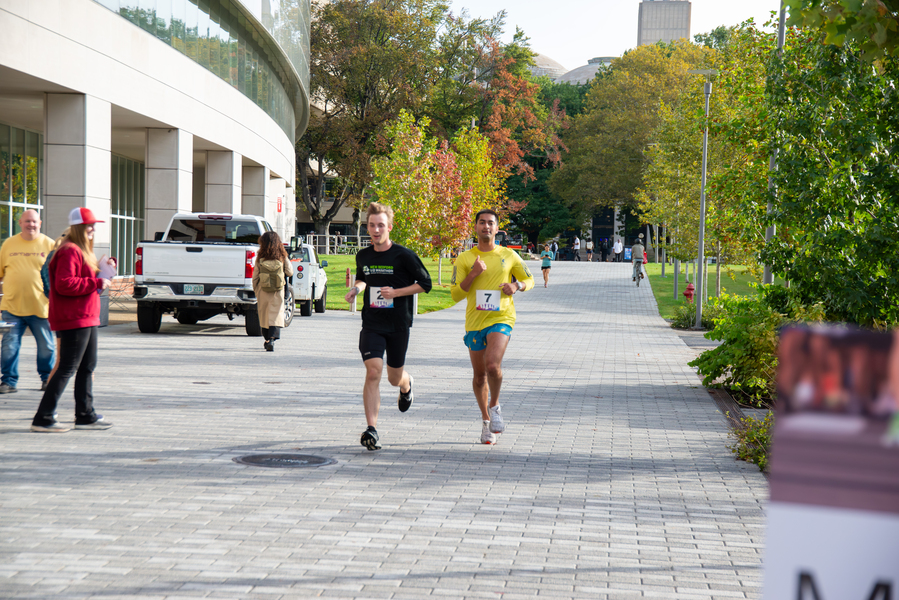Two MIT students run past a campus building toward the finish line.
