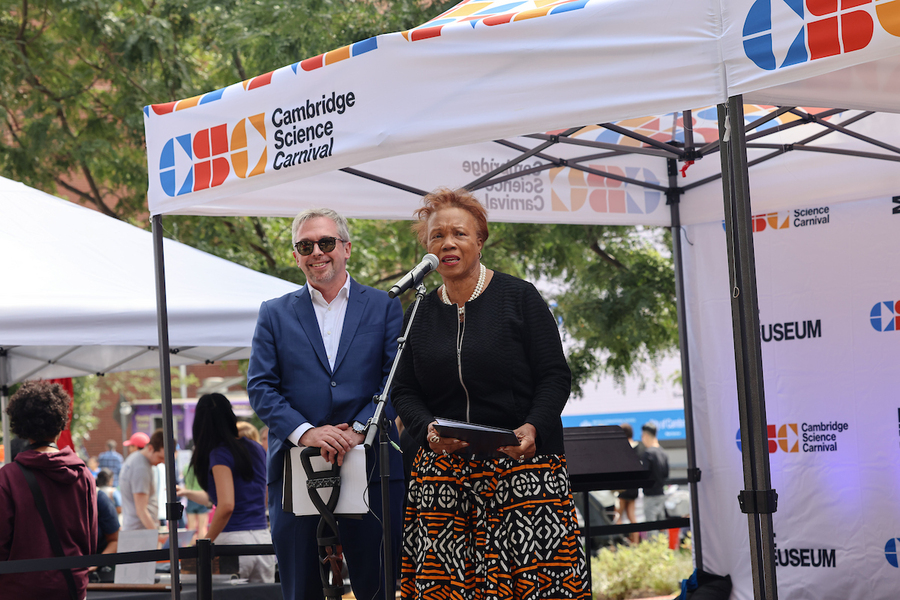 Denise Simmons stands at a podium beneath a small tent, with Michael John Gorman standing next to her