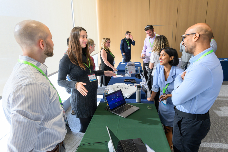 Four people stand around a table, talking. There are two more tables behind them with people milling about