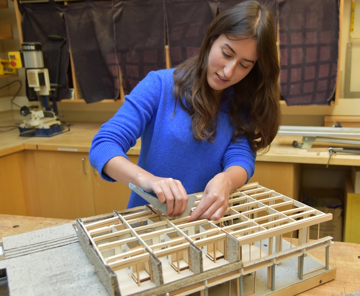 Aleks Banaś uses sandpaper on wooden model of a building frame