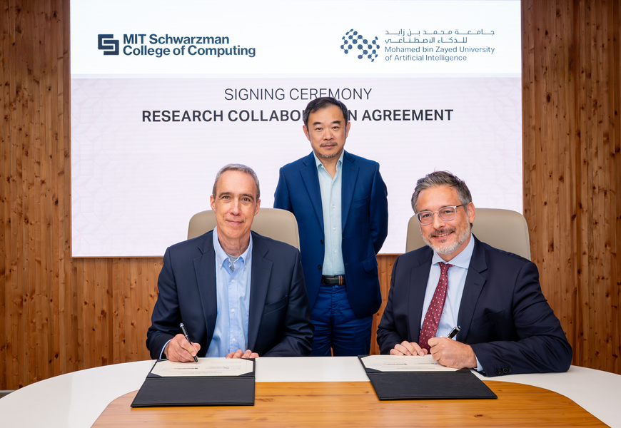 Dan Huttenlocher and Sami Haddadin, seated at a table, sign an agreement, with Eric Xing standing behind them