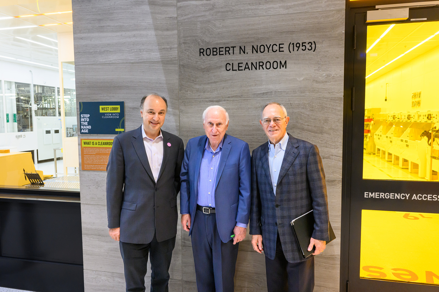 Three men in suits stand in front of a yellow window.