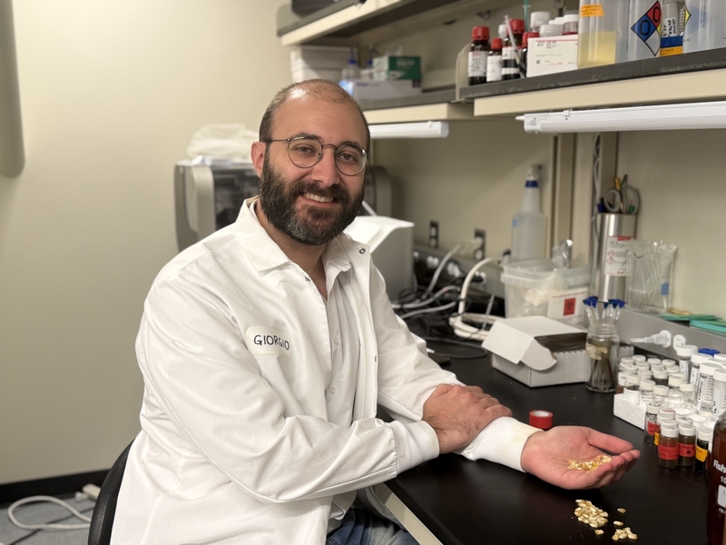 Giorgio Rizzo poses for a photo at a lab bench, while holding a handful of seeds
