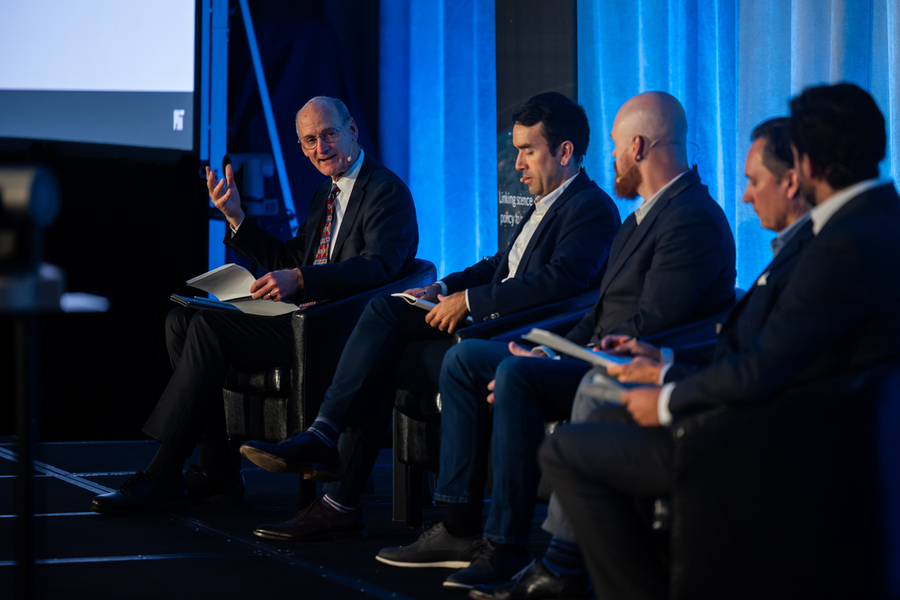 Five men sit on a dimly lit stage in conversation. 