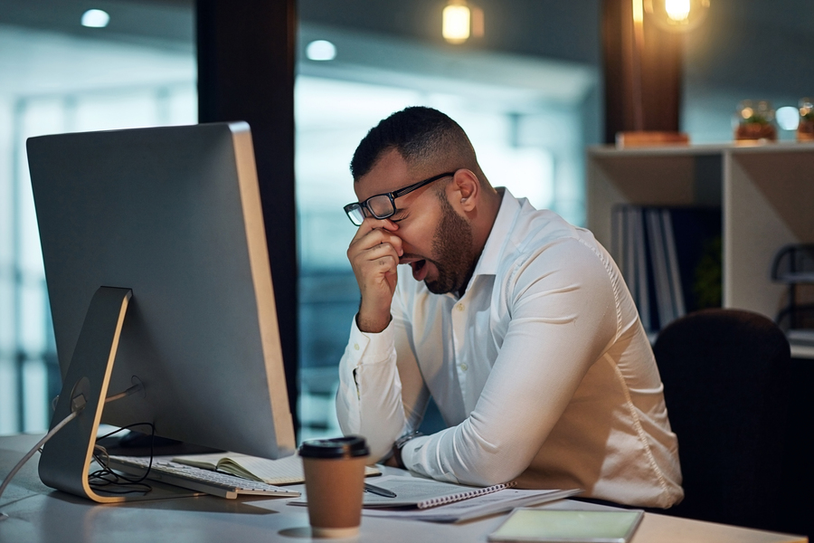 A tired man yawning in front of his computer
