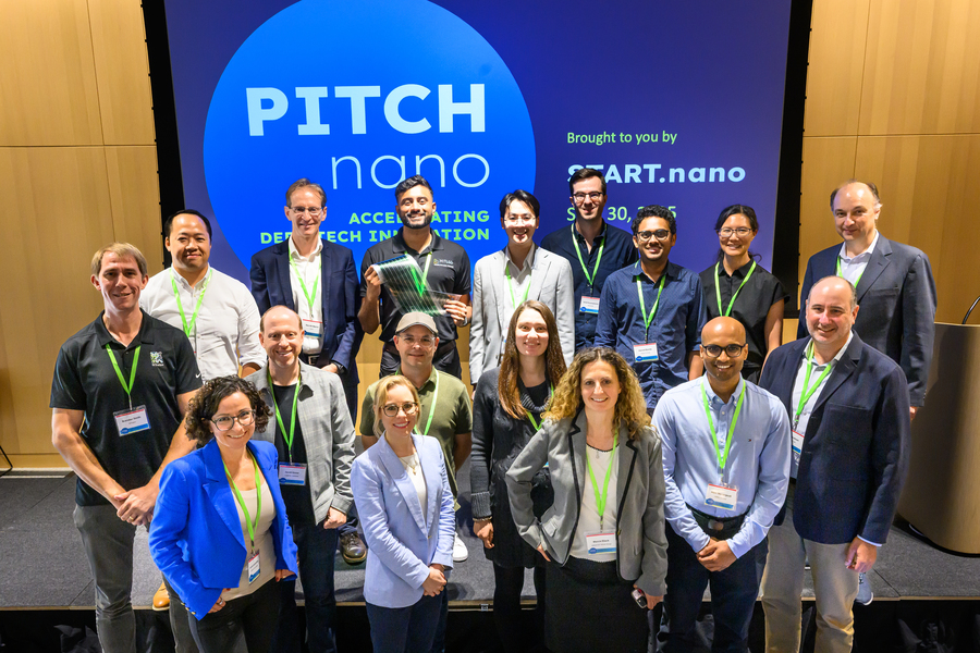 17 people pose on a small stage with "Pitch nano" on a screen behind them