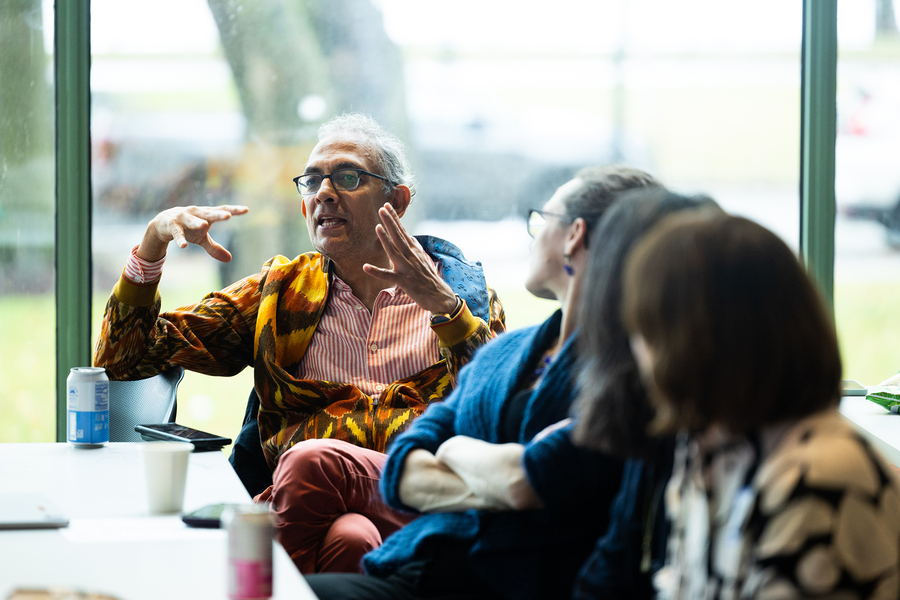 Abhijit Banerjee, seated at a table in front of a large window, speaks while several others look on.