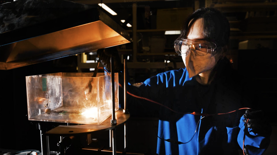 Hyein Choi, wearing a face mask, examines a glowing research experiment in a darkened lab