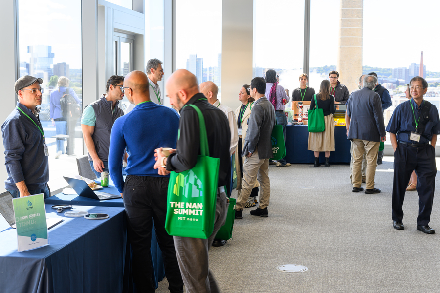 A room with tables arranged along its perimeter holds people talking to each other. About 20 individuals are visible.