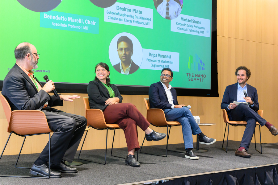 Four people sit in a row, talking on a stage, beneath a projected slide that identifies them.