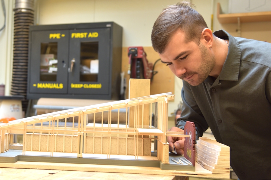 Vincent Jackow uses tweezers to move pieces of wood on model of building frame