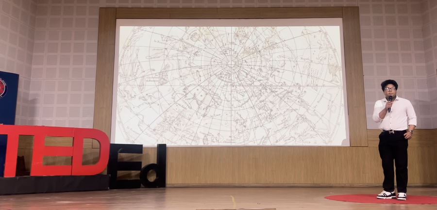 Vivan Mirchandani speaks in front of a screen, which shows graphics of constellations. A "TEDEd" sign is at left.