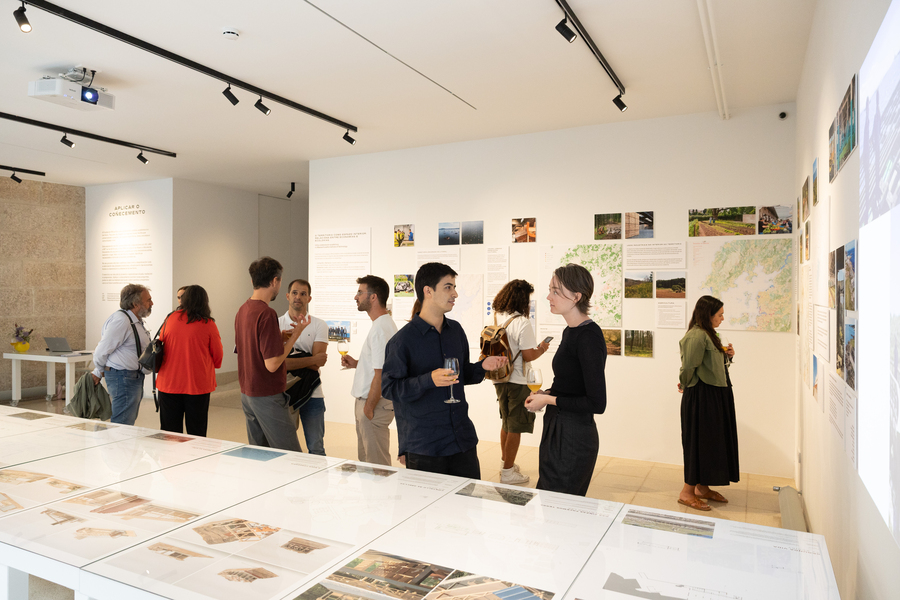 People looking at documents at an indoor exhibition. Several hold glasses of wine.