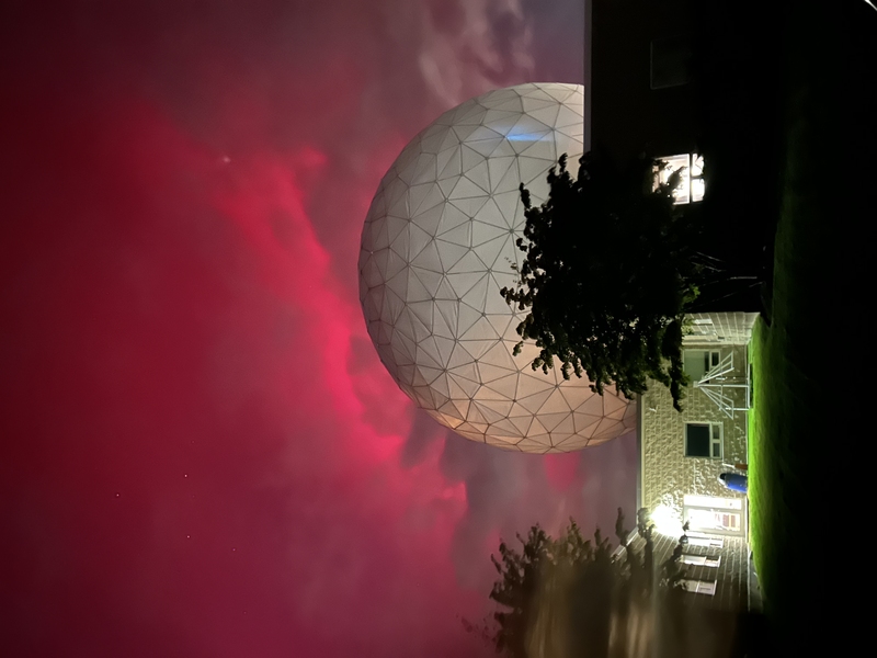 Pink aurora behind a large white geodesic dome on a dark, single-story building