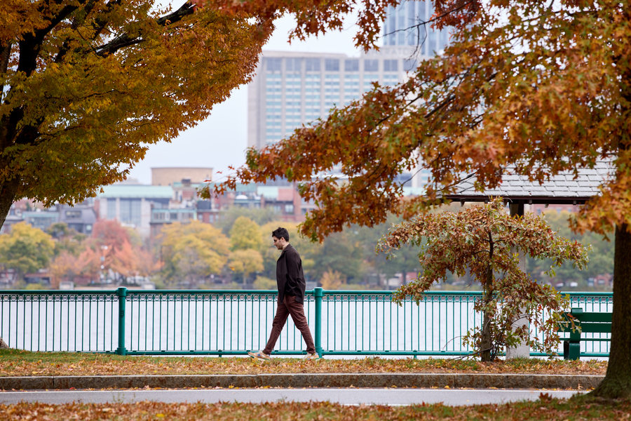 Ben Manning walks along Charles River esplanade on an overcast day with tree leaves in fall colors