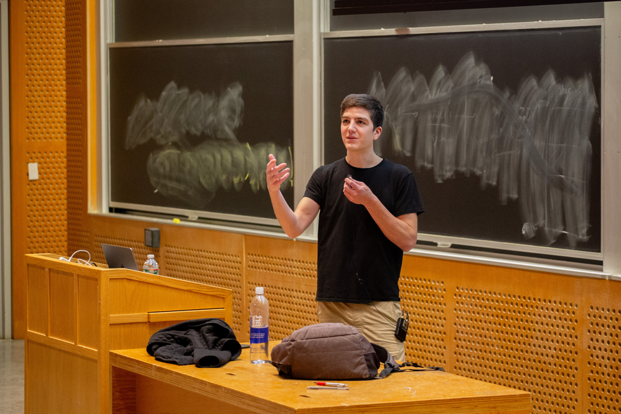 Hannes Stärk stands behind a desk, speaking in front of an erased chalkboard in a lecture hall.