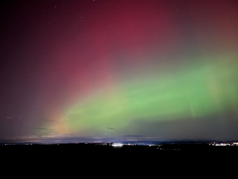 Pink and green aurora with stars visible over a town's lights at the bottom of the image