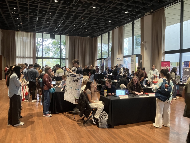 Students mill about a large room with numerous staffed tables with black tablecloths.