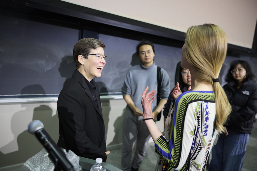 Jennifer Lewis speaks to a person with a ponytail next to a blackboard as three other people look on