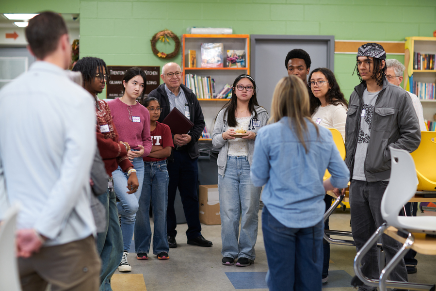About a dozen people standing in a semicircle look intently at someone whose back is to the camera
