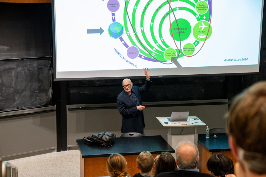 Diran Apelian stands before an audience, pointing to a slide illustrating a framework for materials discovery that emphasizes reuse and recycling.