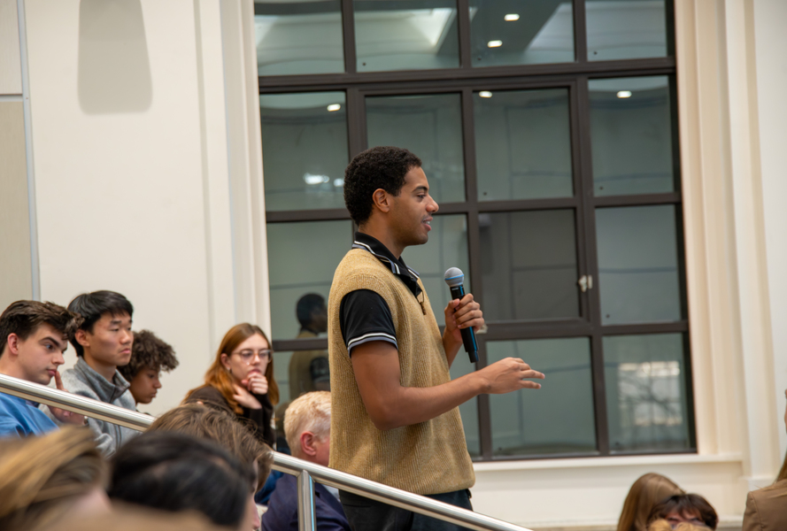 A student in a lecture hall stands holding a microphone to ask a question