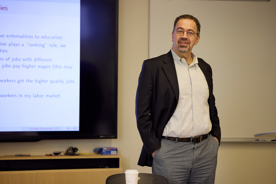Daron Acemoglu stands in front of projector screen and wall