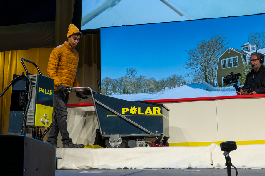 A student demonstrates how to use a small zamboni roughly the size of a walk-behind lawnmower