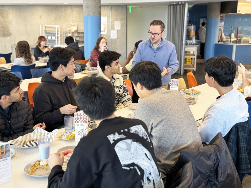 Andrew Mankus talking with a group of students sitting at a table