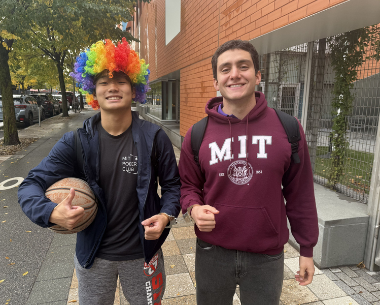 Two students standing outside, handcuffed together, one wearing a rainbow colored wig and the other a MIT sweatshirt.