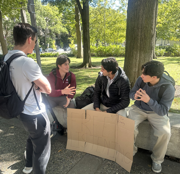 Four students sitting outside with a crude cardboard sign that reads "Free Listening for charity"