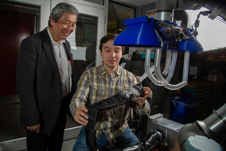 Kentaro Barhydt holds a vine prototype made of black fabric next translucent plastic arms of the vine robot.