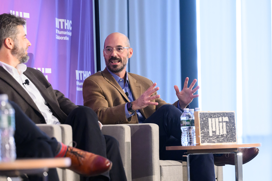 On a stage, Mike Tarkanian is speaking and Will Broadhead is listening. Both are seated.