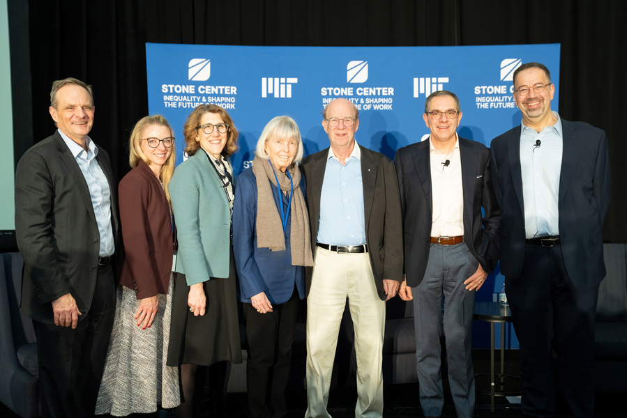 Seven people stand smiling in front of a blue MIT Stone Center backdrop