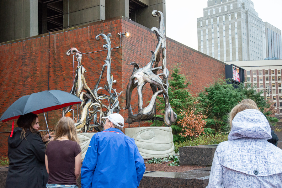 Four people view the 19-foot-tall sculpture ‘Amulet’ on a cool, rainy day.