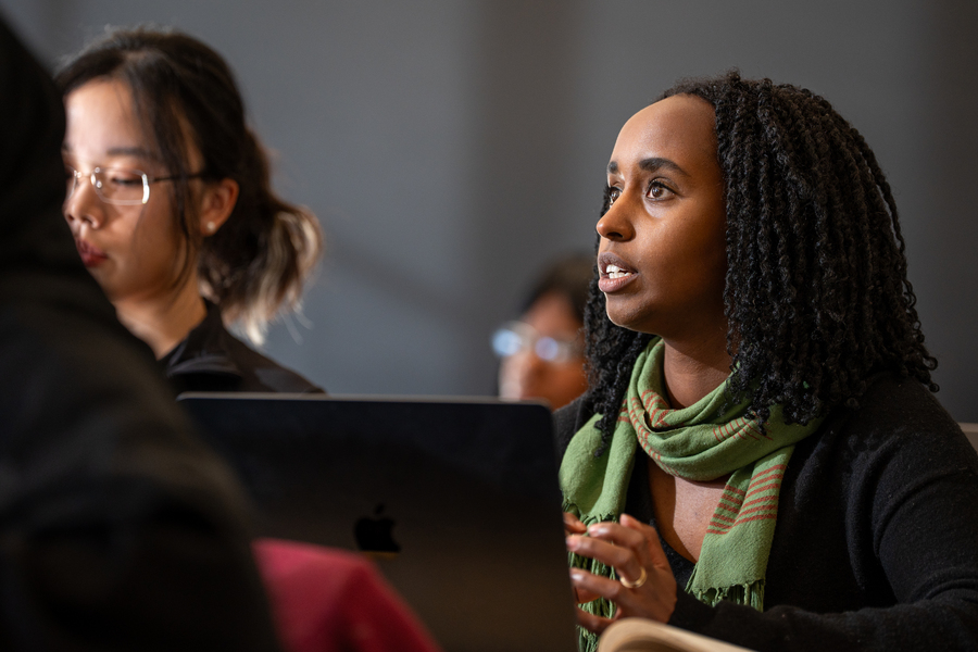 A student sitting at an open laptop answers a question in a class.