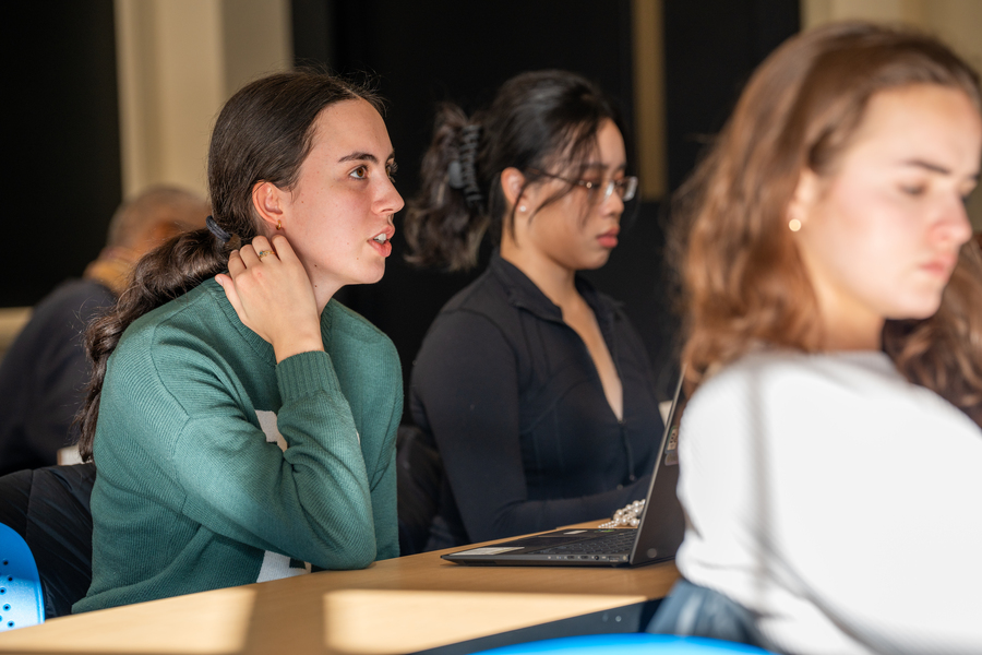 Closeup of a student speaking, with two others around her, seated in a classroom