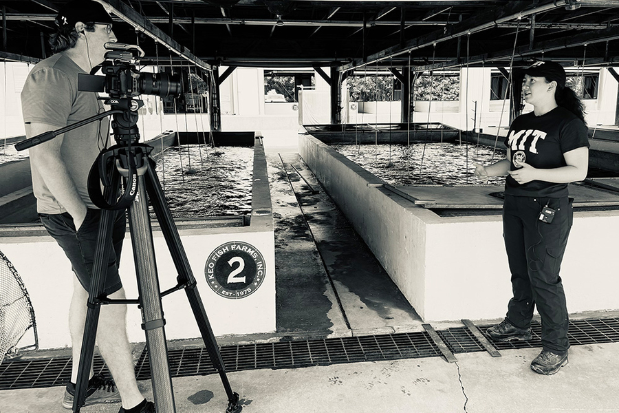 Grayscale photo of a man with a camera on a tripod talking to Kik Hayano, who stands before two raised pools.