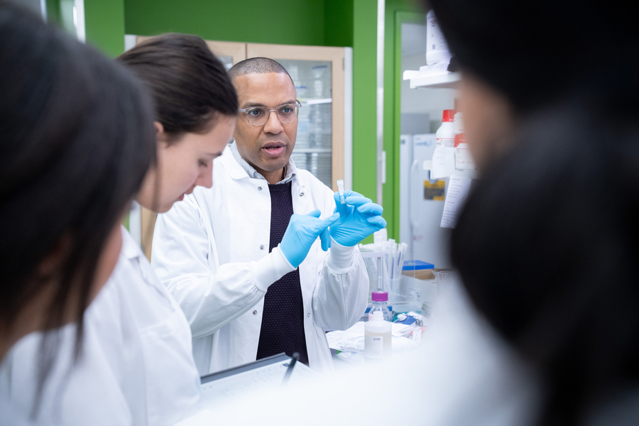 Bryson holds a small pipette while talking to students in lab.