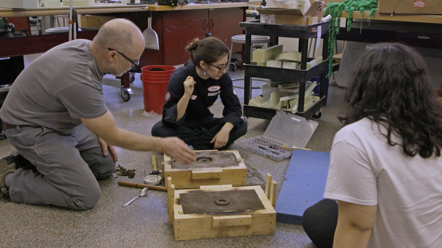 An instructor kneels on the floor with two students