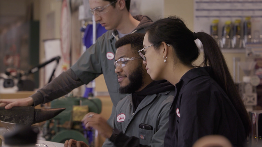 Three students huddle side by side, focused on something out of the frame