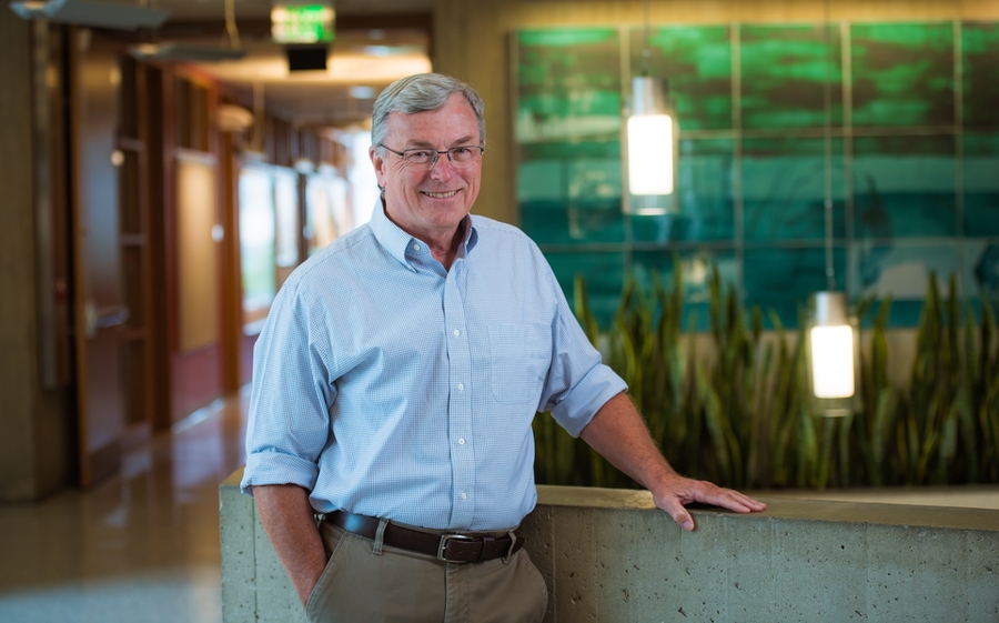 T. Alan Hatton poses, standing, in a colorful indoor hallway