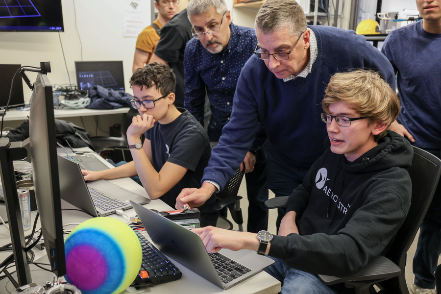 Nicholas Roy and Jonathan How look over a laptop together with students in a technology lab 