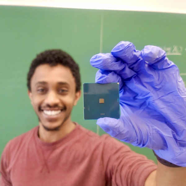 Natnael Kahssay, wearing nitrile gloves, smiles and holds up a computer chip for the camera.
